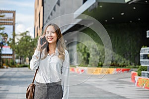 Asian business female calling on smart mobile phone and walking on street outside office building