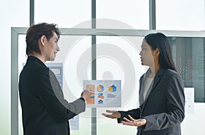 Asian business man and woman looking at paper note stick on glass board to discuss and working in office