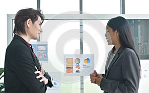 Asian business man and woman looking at paper note stick on glass board to discuss and working in office