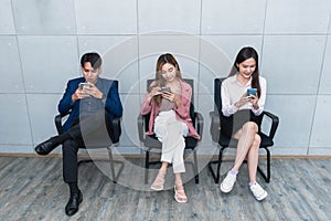 Asian business man and woman sitting and using a mobile phone against the background of a cement wall.