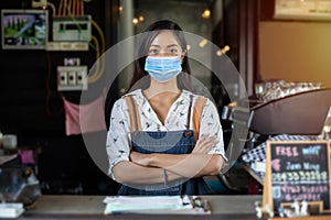 Asian business owner and barista wearing face mask and smiling after reopening coffee shop