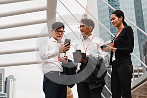 Asian business people with tablet and smartphone on hands standing and having business conversation outdoors urban