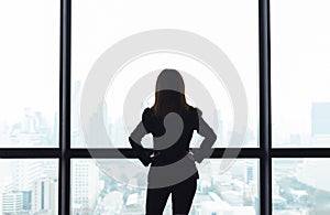 Asian business woman with arms akimbo looking out the window at city view background