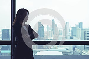 Asian business woman crossed arms looking out the window at city view background