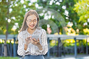 Asian business woman happy smiling looking at smartphone standing park outdoor green nature background