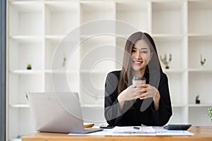 Asian business woman holding a cup of coffee at the desk Financial graph with desktop and laptop calculator for office