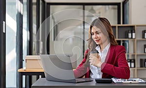 Asian business woman holding a cup of coffee at the desk Financial graph with desktop and laptop calculator for office