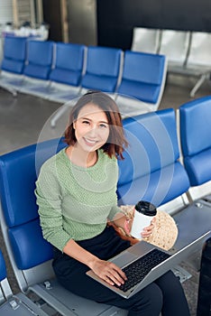 Asian business woman in international airport terminal, working on her laptop while waiting for flight