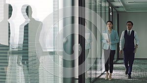 Asian business woman and man walking in a hurry in office hallway