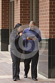 Asian business woman and man walking and talking with tablet