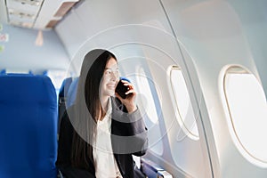 Asian business woman passenger sitting on business class luxury plane while working using smart phone mobile talking or