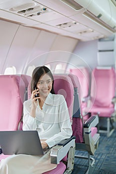 Asian business woman passenger sitting on business class luxury plane while working using smart phone mobile talking or