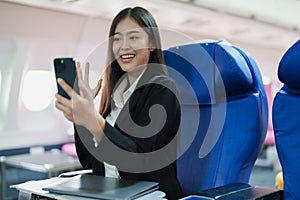 Asian business woman passenger sitting on business class luxury plane while working using smart phone mobile talking or