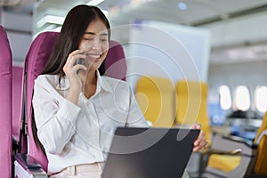 Asian business woman passenger sitting on business class luxury plane while working using smart phone mobile talking or