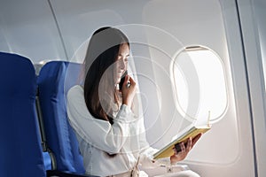 Asian business woman passenger sitting on business class luxury plane while working using smart phone mobile talking and