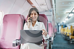 Asian business woman passenger sitting on business class luxury plane while working using smart phone mobile talking or