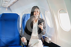 Asian business woman passenger sitting on business class luxury plane while working using smart phone mobile talking or