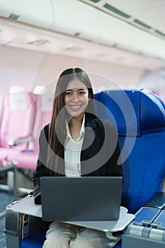 Asian business woman passenger sitting on business class plane while working on laptop computer with simulated space