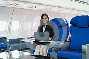 Asian business woman passenger sitting on business class plane while working on laptop computer with simulated space