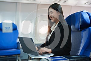 Asian business woman passenger sitting on business class plane while working on laptop computer with simulated space