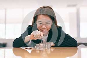 Asian business woman putting coin on pile of money on table in office interior background