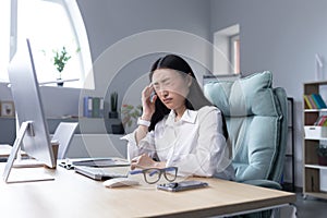 Asian business woman sick working in office, having severe headache, holding hands on head in depression and sad