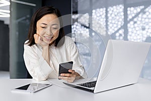 Asian business woman smiling and working at the workplace inside the office, businesswoman reading news using smartphone