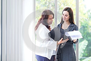 Asian business woman stands and talk to another to consult about work intently in office