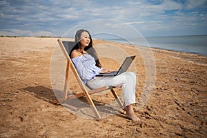 Asian business woman with tablet computer during tropical beach vacation. Freelancer working on laptop lying on sun lounger.