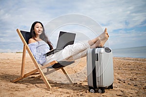 Asian business woman with tablet computer during tropical beach vacation. Freelancer working on laptop lying on sun lounger.