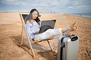 Asian business woman with tablet computer during tropical beach vacation. Freelancer working on laptop lying on sun lounger.