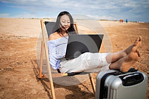 Asian business woman with tablet computer during tropical beach vacation. Freelancer working on laptop lying on sun lounger.