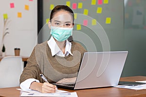 Asian business woman use labtop and note job on paper in office