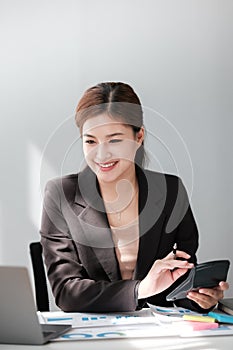 Asian Business woman using calculator and laptop for doing math finance on an office desk, tax, report, accounting