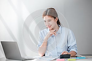 Asian Business woman using calculator and laptop for doing math finance on an office desk, tax, report, accounting
