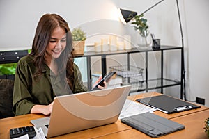 Asian business woman using laptop checking smartphone indoors home office