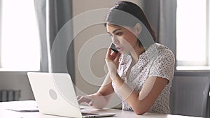 Asian business woman using laptop talking on phone in office