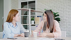 Asian business women enjoying drinking warm coffee, discuss about work and chit chat gossip while relax working in office. Smart