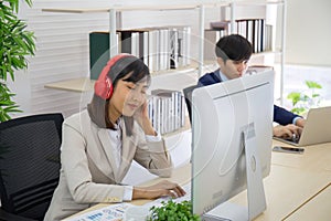 Asian business women listening to music from headphones in the office