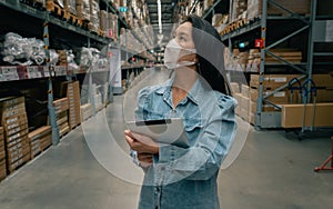 Asian business working woman wear mask using digital tablet checking stock of products in warehouse