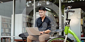 Asian businessman with bicycle using laptop and sitting outside the office building. man commuting on bike go to work