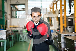 Asian businessman with boxing gloves in factory ready to fight