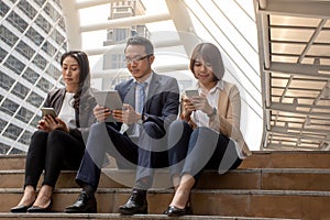 Asian businessman and businesswomen discussing ideas with digital mobile phone while sitting at the stairs