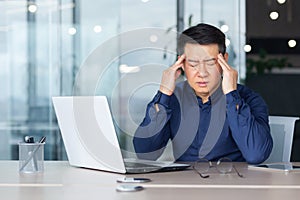 An Asian businessman feels severe headache, Holds his head with his hands
