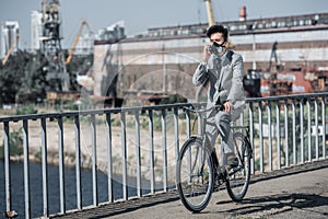 asian businessman in gas mask riding bicycle on bridge and talking by smartphone air