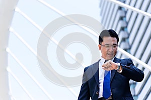 The asian businessman has holding a black bag and looking on watch in hurrying time.