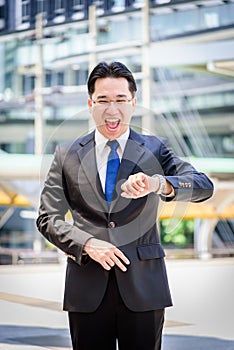 The asian businessman has holding a black bag and looking on watch in hurrying time.