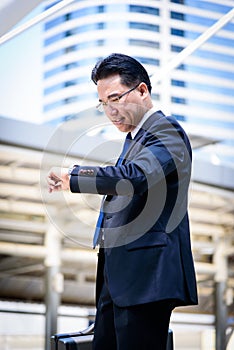 The asian businessman has holding a black bag and looking on watch in hurrying time.