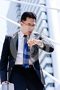 The asian businessman has holding a black bag and looking on watch in hurrying time.