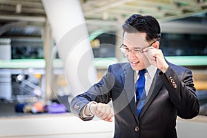 The asian businessman has holding a black bag and looking on watch in hurrying time.